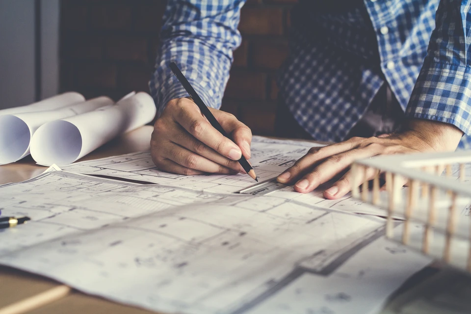 Homme en chemise à carreaux bleus travaillant sur des plans architecturaux étalés sur une table