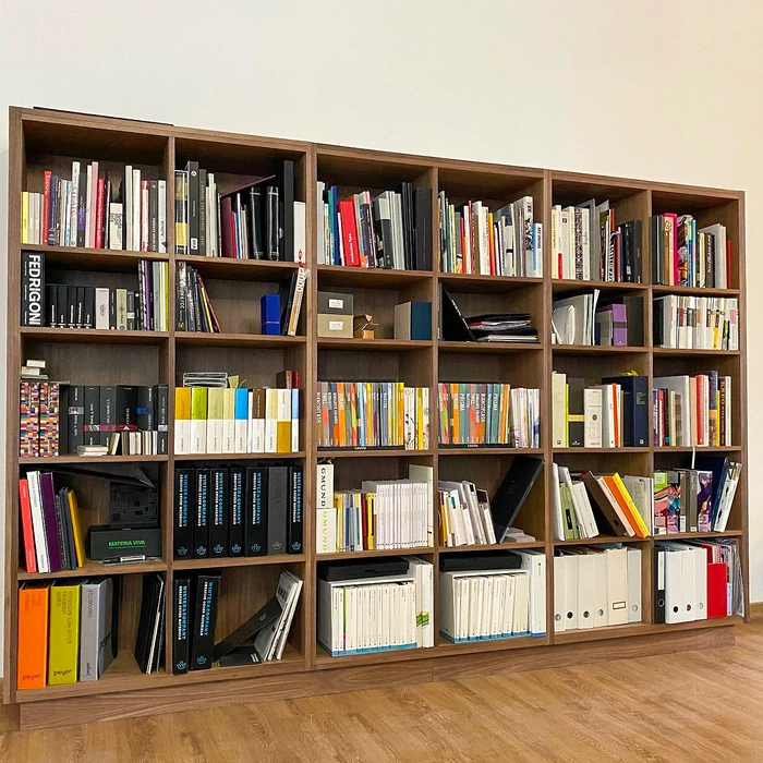 Grande bibliothèque modulaire en bois foncé, remplie de livres, catalogues et échantillons de papier professionnels