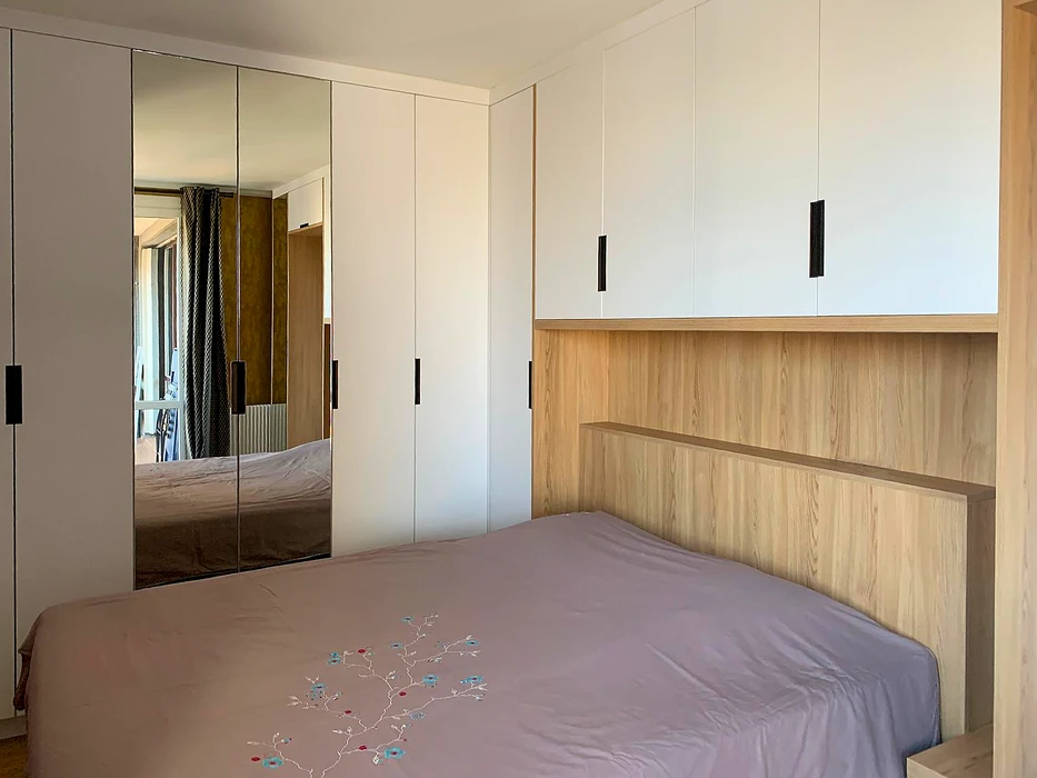 Chambre à coucher moderne avec lit double, tête de lit en panneau mélaminé décor chêne naturel, surmonté de rangements hauts à portes battantes blanc mat avec poignées noires en T