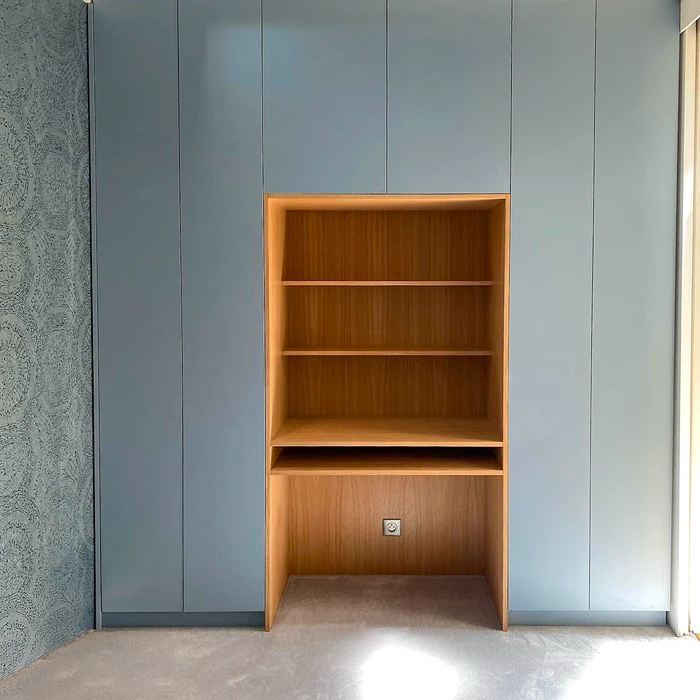 Bibliothèque encastrée en bois de teck clair, intégrée dans un meuble mural sur mesure laqué bleu-gris mat