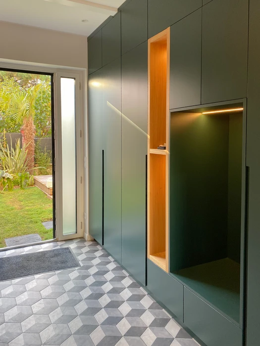 Entrée contemporaine avec mur de rangements sur mesure en MDF laqué vert sapin mat, intégrant des niches en contreplaqué chêne naturel éclairées par bandeau LED