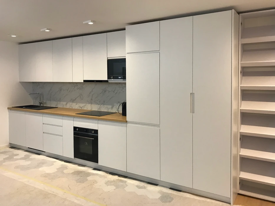 Cuisine linéaire moderne entièrement équipée, façades laquées blanc mat sans poignées, plan de travail en bois naturel