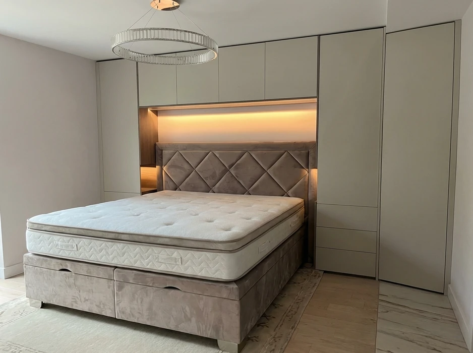 Chambre à coucher moderne avec lit coffre double, tête de lit capitonnée en velours taupe à motifs losanges, éclairage LED indirect ambré encastré